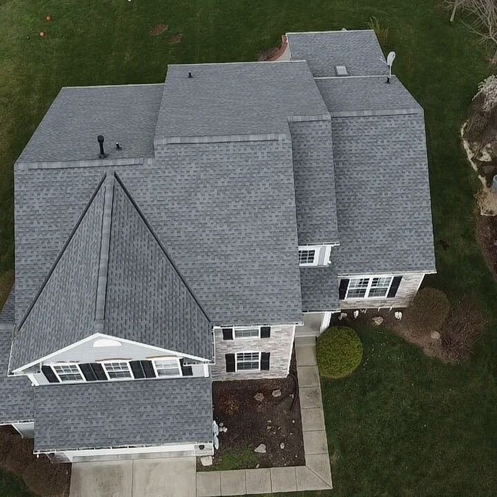 Overhead drone view of a large two-story house with a new grey shingle roof