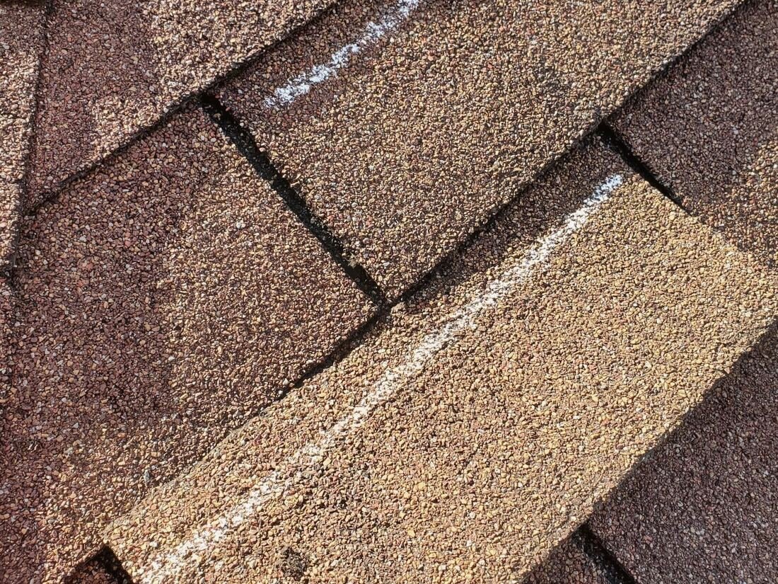 Close-up of a brown shingle with chalk marks from a roof inspection