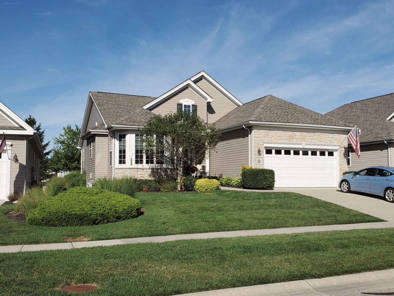 Two-story home with beige siding and a finished grey shingle roof, front lawn in summer