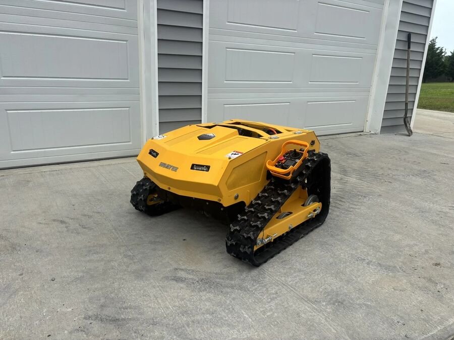 Small orange tracked remote control mower sitting on a concrete pad