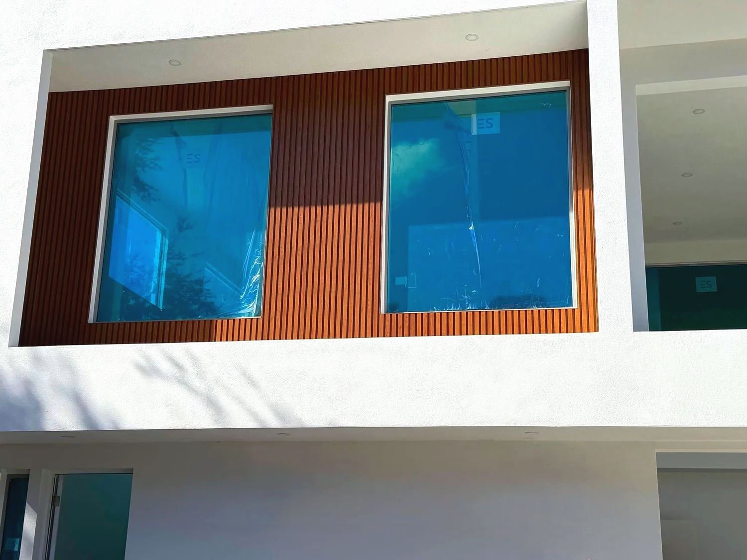 Close-up of wood-look vertical aluminum cladding framing two second-floor windows on a white stucco house