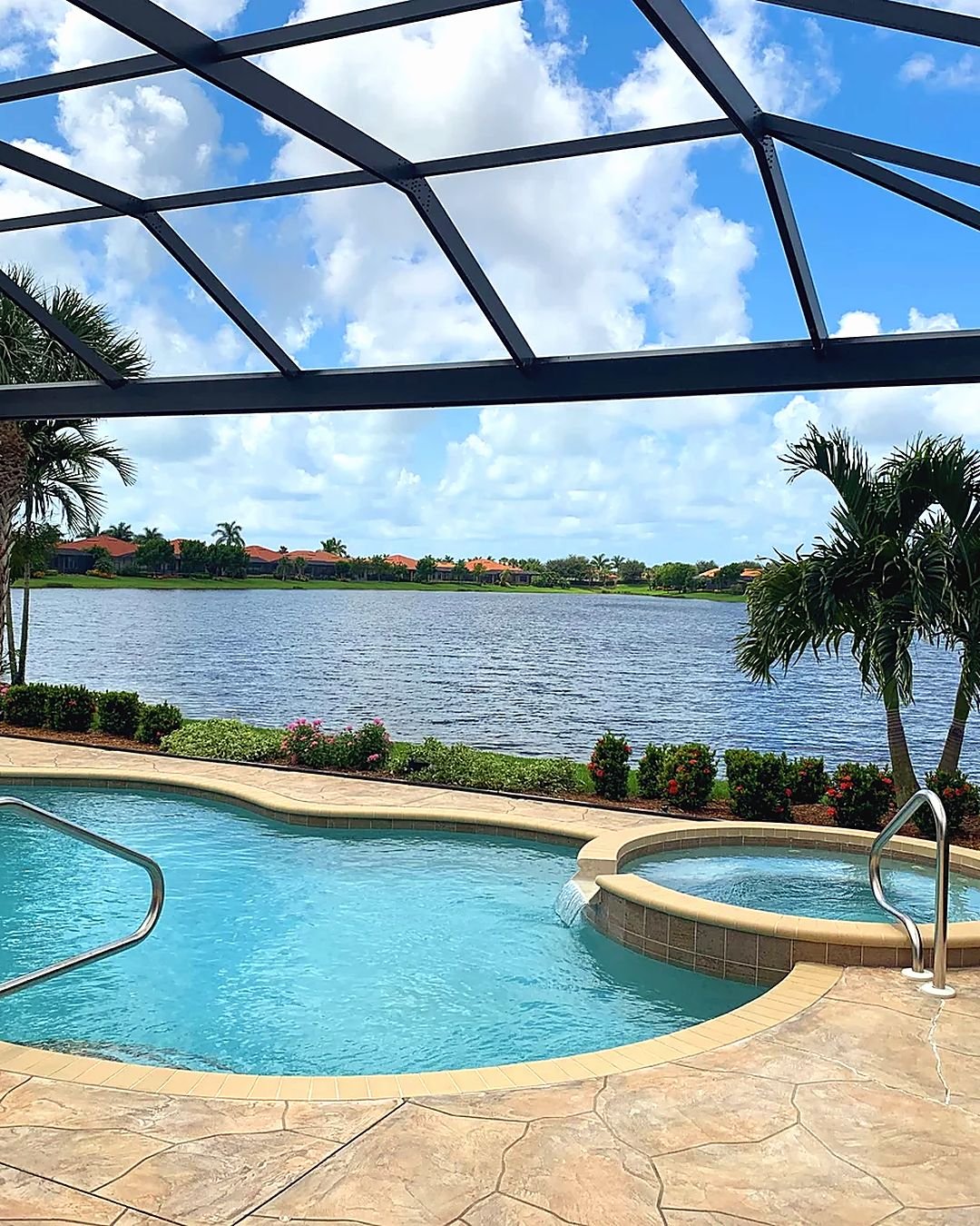Black aluminum pool cage over a pool and spa on a Southwest Florida lake, palms and clouds beyond the screen
