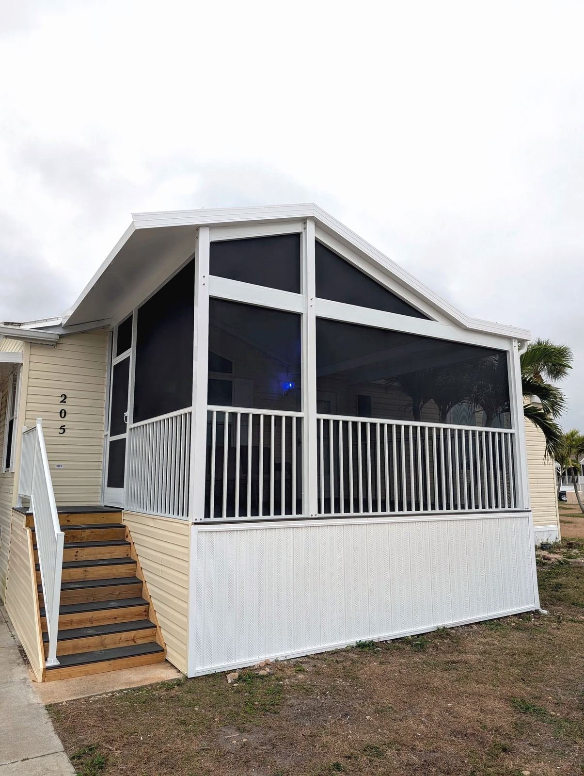 Raised white screen room with a gable roof and white railing on a manufactured home, wood steps to the door, Southwest Florida