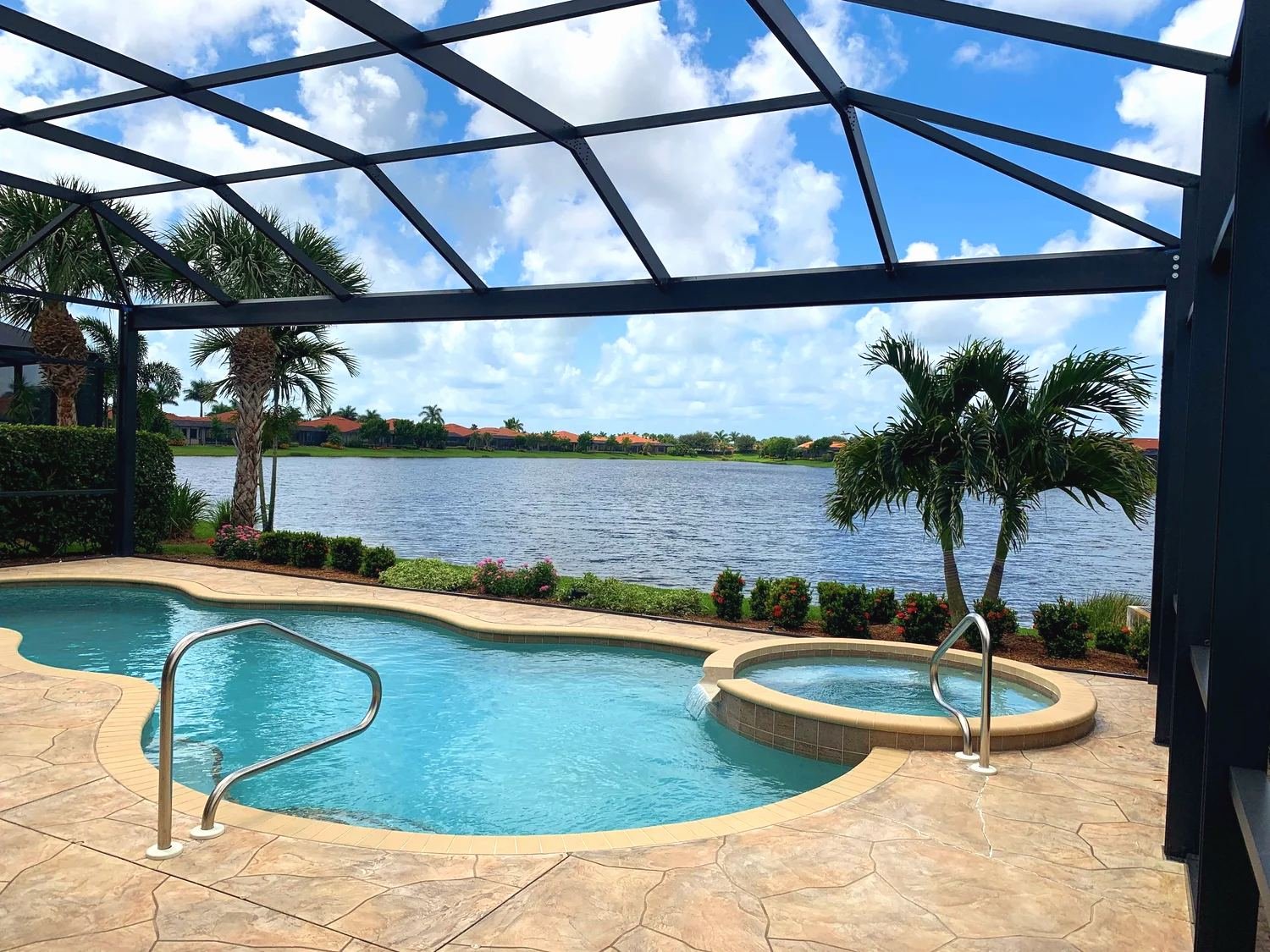 Black aluminum pool cage over a pool and spa on a Southwest Florida lake, palms and clouds beyond the screen