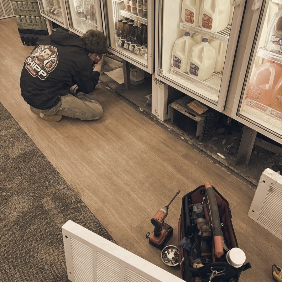 Shipp's tech kneeling at a row of glass-door commercial coolers in a store